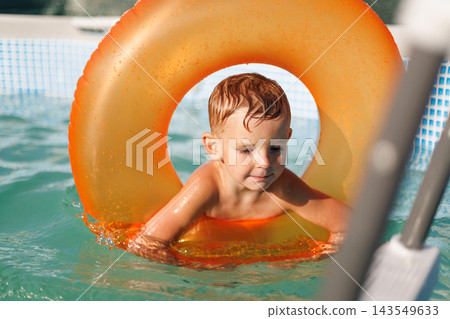 Young boy swimming with inflatable ring in outdoor pool Young boy swimming with inflatable ring in outdoor pool 143549633