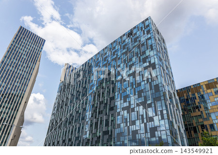 Low angle view of contemporary glass architecture under blue sky and white clouds Low angle view of contemporary glass architecture under blue sky and white clouds 143549921