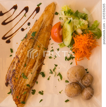 Fried plaice with canarian potatoes and vegetable salad on a plate 143550205