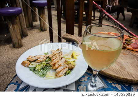 Pizza and Caesar salad on a mosaic table on a pub terrace bathed in bright sunlight, in the suburbs of London. Pizza and Caesar salad on a mosaic table on a pub terrace bathed in bright sunlight, in the suburbs of London. 143550889