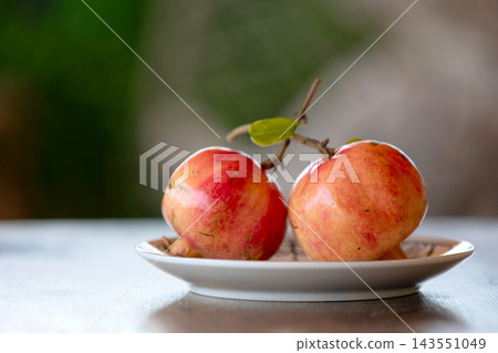 Two fresh ripe pomegranates on a plate on wooden table with soft bokeh background 143551049