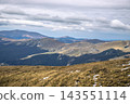 Autumn landscape with gold valley and winding trail through mountainside under dramatic sky 143551114