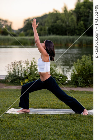 Woman in Crescent Lunge on a Dock by the Lake. A young Hispanic woman practises a crescent lunge on a wooden dock over the calm lake at sunset, embracing an active and mindful lifestyle. Woman in Crescent Lunge on a Dock by the Lake. A young Hispanic woman practises a crescent lunge on a wooden dock over the calm lake at sunset, embracing an active and mindful lifestyle. 143552409