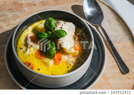 Creamy Waterzooi With a White Fish Fillet and Carrot. Hearty close up of creamy Belgian waterzooi with a fillet of white fish, carrot and potato in a golden broth, garnished with basil and black peppe 143552472