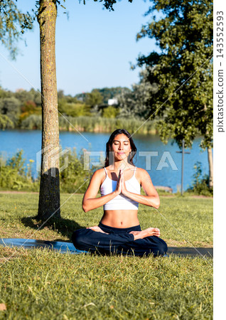 Woman in Seated Meditation With Prayer Hands in the Park at Sunset. A young Hispanic woman practises seated meditation with prayer hands surrounded by greenery in a park at golden hour, promoting bala Woman in Seated Meditation With Prayer Hands in the Park at Sunset. A young Hispanic woman practises seated meditation with prayer hands surrounded by greenery in a park at golden hour, promoting bala 143552593