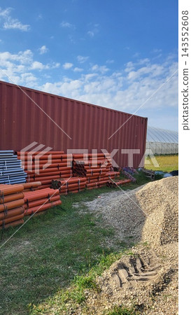 Plastic pipes for the irrigation system of a farm's greenhouse next to a storage container for materials, agricultural transport and a warehouse for packaging materials. Plastic pipes for the irrigation system of a farm's greenhouse next to a storage container for materials, agricultural transport and a warehouse for packaging materials. 143552608