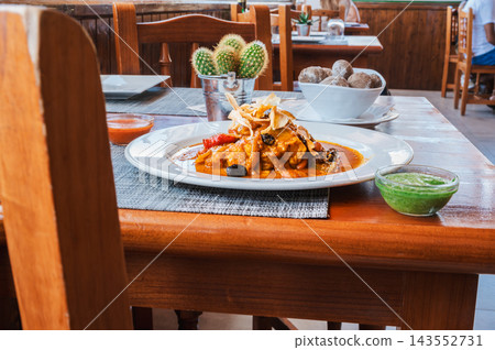 Canarian cod on a table in a bright island restaurant. A plate of cod in tomato broth waits on a laid table in a bright Canarian restaurant dining room. Everyday island gastronomy for travel hospitali 143552731