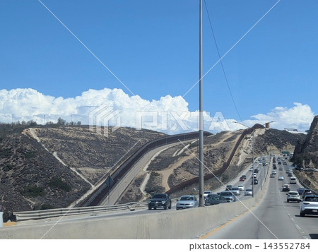 在蒂華納，墨西哥邊境高速公路上排著長長的車隊，美國邊境牆高聳於山丘之上，構成了一幅獨特的景觀。 143552784