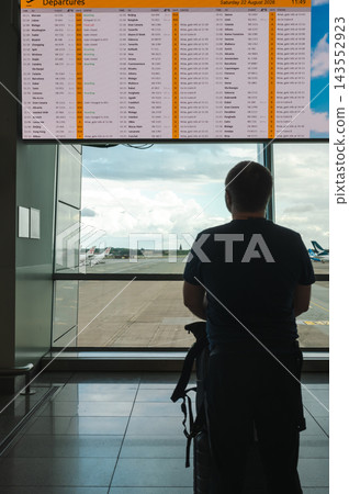 Traveler silhouetted against the airport apron. A man stands almost in silhouette against the bright glass of an airport apron view. Strong backlight turns an ordinary wait into a graphic travel momen Traveler silhouetted against the airport apron. A man stands almost in silhouette against the bright glass of an airport apron view. Strong backlight turns an ordinary wait into a graphic travel momen 143552923