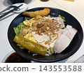 Rows of black buffet trays display sliced meat with lettuce, yellow sauce, crispy onion topping, and serving spoons. 143553588