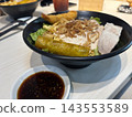 Rows of black plates hold assorted sushi rolls beside a white bowl of dark dipping sauce. 143553589