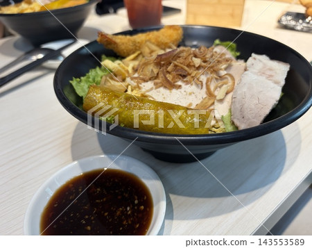 Rows of black plates hold assorted sushi rolls beside a white bowl of dark dipping sauce. 143553589