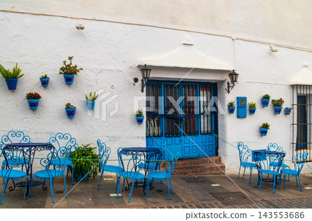 Cozy street terrace with blue tables and chairs and hanging flower pots in the historic white village of Mijas, Andalusia, Spain Cozy street terrace with blue tables and chairs and hanging flower pots in the historic white village of Mijas, Andalusia, Spain 143553686
