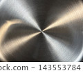 Close-up of circular brushed stainless steel with fine concentric grain and a bowtie-shaped pattern of warm golden highlights and dark sectors 143553784