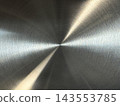 Close-up of polished metal surface with fine circular brushed texture and two diagonal golden-white light beams converging at a central point 143553785