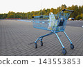Metal shopping cart with a plastic bag inside stands on a paved parking lot outside a supermarket 143553853