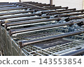 Long row of metal shopping carts with black handles stands parked outside supermarket store. Retail business, consumer commerce, and grocery shopping service concept. 143553854