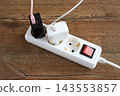 White extension power strip with plugged-in charger adapters and red toggle switch lies on wooden surface. Demonstrates the concept of energy saving and efficient electricity 143553857