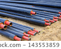 Stack of steel heating pipes resting on sand. Black insulated pipeline installation for utility system modernization, heating system installation, and construction supplies 143553859