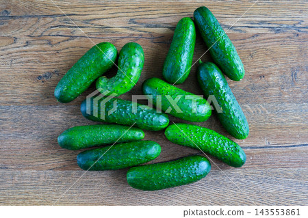 Fresh green whole cucumbers lie scattered on dark wooden surface. Healthy eating, organic farming, and raw agricultural food Fresh green whole cucumbers lie scattered on dark wooden surface. Healthy eating, organic farming, and raw agricultural food 143553861