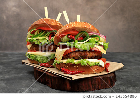 Two double cheeseburgers with fresh lettuce, tomato, cream cheese, cucumber, onion, chili pepper and a patty on an old wooden board,food delivery concept,menu and advertising for cafes and restaurants Two double cheeseburgers with fresh lettuce, tomato, cream cheese, cucumber, onion, chili pepper and a patty on an old wooden board,food delivery concept,menu and advertising for cafes and restaurants 143554890