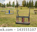 Empty Child Swing in Quiet Park Playground With Grass and Distant Equipment 143555107
