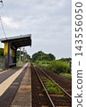 A quiet rural unmanned station platform surrounded by trees and plants, and a single-track railway line. 143556050