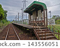 A quiet rural unmanned station platform surrounded by trees and plants, and a single-track railway line. 143556051