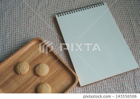 Flat lay of cookies on wooden plate beside blank notepad with copy space  143556506