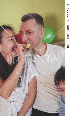 Husband eating a chip from his wife's hand. Playful love, trust and family humor. Husband eating a chip from his wife's hand. Playful love, trust and family humor. 143556941
