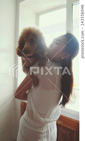 Woman holding a fluffy poodle close to her face. Love, tenderness and pet therapy. 143556946