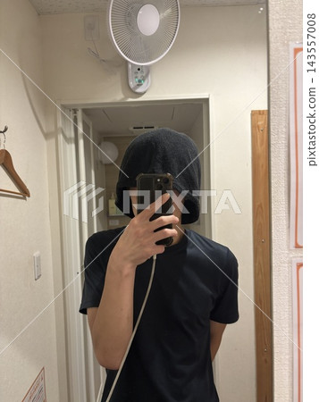 一名男子戴著桑拿帽,對著鏡子拿著智慧型手機。 一名男子戴著桑拿帽,對著鏡子拿著智慧型手機。 143557008