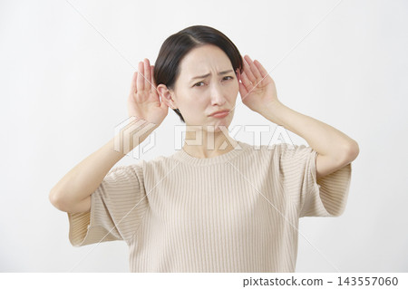 一名女子將手放在耳朵上，試圖聽清楚聲音，背景是白色的。 143557060