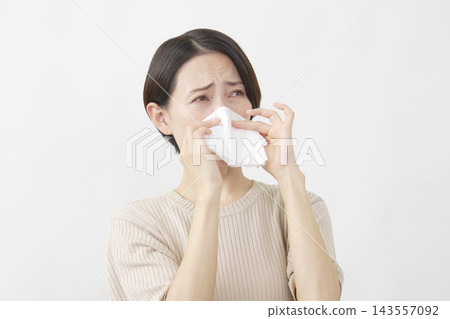 一位四十多歲的女性在白色背景前用紙巾擤鼻涕。 143557092