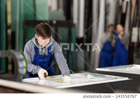 Young man employee in blue overall measures given length of plastic material Young man employee in blue overall measures given length of plastic material 143558767
