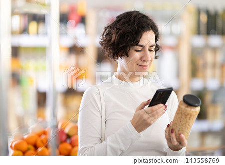 Woman get acquainted with product, scan QR code, take reading beans label using phone camera in shop Woman get acquainted with product, scan QR code, take reading beans label using phone camera in shop 143558769