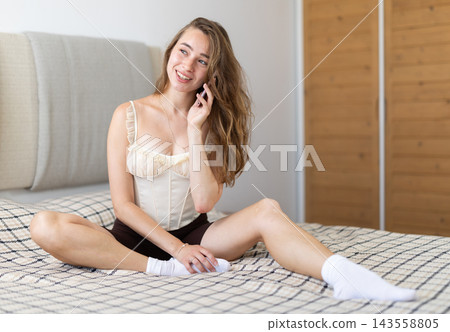 Young woman talking on smartphone sitting on bed 143558805