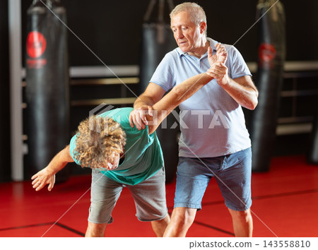 Elderly man learning self-defense grips and escapes at gym Elderly man learning self-defense grips and escapes at gym 143558810