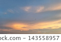 A blurred dragonfly flies through a blue and orange sunset sky filled with soft clouds 143558957