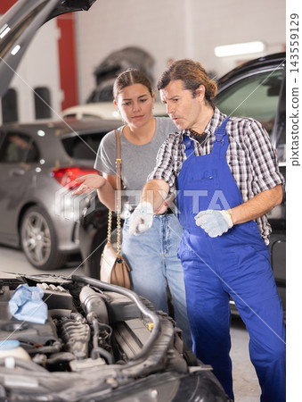Mechanic consults woman on repairs under hood of car Mechanic consults woman on repairs under hood of car 143559129