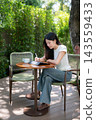 Asian Woman Writing on Tablet with Stylus at Garden Patio Table 143559433