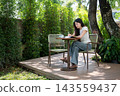 Asian Woman Using Stylus on Digital Tablet at Garden Terrace Table 143559437