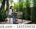 Asian Woman Drinking Coffee with Eyes Closed at Garden Cafe Table 143559438
