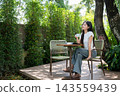 Asian Woman Holding Coffee Cup Looking Peaceful on Garden Patio 143559439