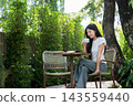 Asian Woman Drinking Coffee with Digital Tablet on Garden Patio 143559440