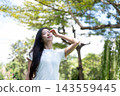 Asian Woman Touching Hair Enjoying Warm Sunlight Outdoors in Park 143559445