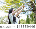 Asian Woman Stretching Arms Upward Towards Sky Outdoors in Park 143559446
