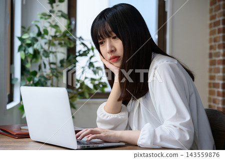 一位日本女性在辦公室裡看著筆記型電腦,陷入沉思。 一位日本女性在辦公室裡看著筆記型電腦,陷入沉思。 143559876