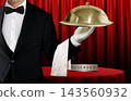 Waiter in black tuxedo holding covered food platter with a cloche in front of reserved table and red curtain 143560932