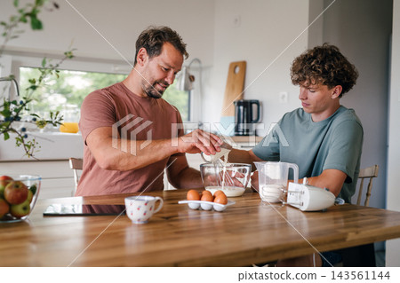 Father and teenage son baking homemade cake in kitchen. Father and teenage son baking homemade cake in kitchen. 143561144